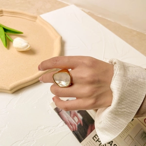 Détail d'une bague dorée de style vintage avec une grande nacre ovale portée au doigt