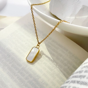 Détail du collier à pendentif rectangulaire en or avec nacre sur un livre ouvert