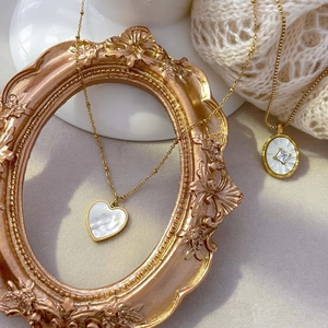 Détail de colliers en cœur nacre et zircons ovales plaqués or 18K sur un tissu blanc