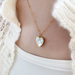 Collier à billes dorées avec pendentif cœur en nacre blanche porté par un mannequin