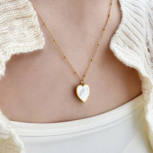 Collier doré avec pendentif cœur en nacre porté sur un tricot blanc élégant