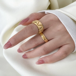 Detail of layered gold rings with geometric triangle texture and vertical stripes on hand