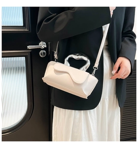Detail of white wave-edge flap crossbody bag with bold silver metal handle on model