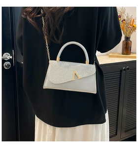 Detail of evening clutch bag with silver sequins and gold chain handle shown by a model