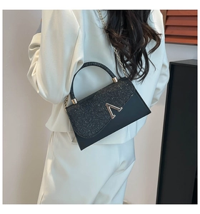 Detail of black crossbody bag with shimmering sequins and gold V metal buckle on model