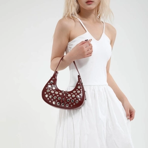 Burgundy hobo shoulder bag with silver rivets shown on a model in a white dress