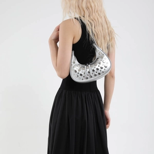 Silver metallic crescent hobo bag with round rivets worn by a model in a black dress