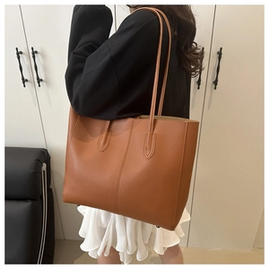Brown leather tote bag on shoulder with decorative stitching and large capacity