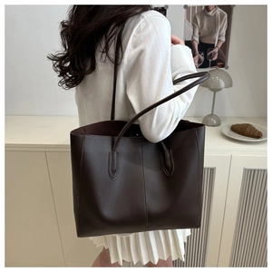 Detail of a dark brown large tote bag with visible vertical stitching and dual slim straps