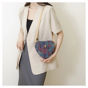 Détail du sac coeur tissé multicolore avec fermoir tête d'aigle sur un tailleur beige