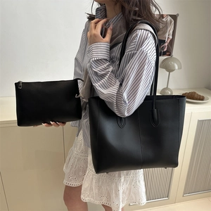 Minimalist large black tote bag with matching pouch shown in a stylish indoor setting