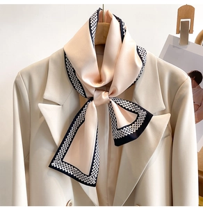 Detail eines Seidenschals mit schwarzem Geometrie-Rand, an beigem Blazer geknotet