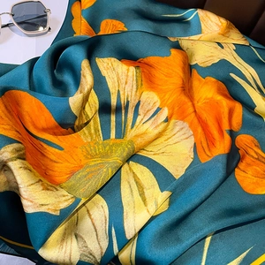 Detailed view of dark green silk scarf with vibrant orange floral prints and satin texture