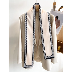 Detail eines cremefarbenen Satin-Schals auf einem beigen Blazer mit gewebter Kante