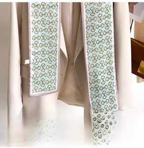 Détail d'un long foulard en soie avec motifs de mors dorés sur un blazer beige