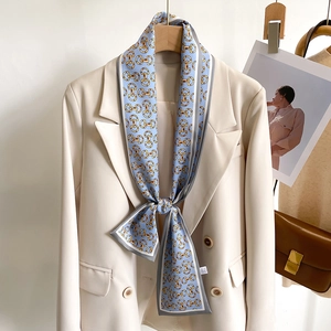 Élégant foulard en soie bleu clair avec motif de chaîne dorée porté sur un blazer blanc