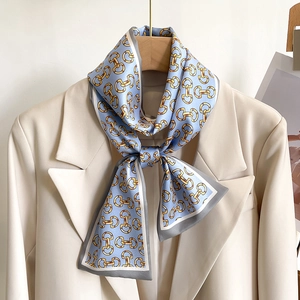Détail d'un foulard étroit en soie bleu clair avec motif de chaîne dorée sur veste beige