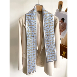 Détail d'un foulard en soie bleu clair à motif mors doré sur un blazer blanc