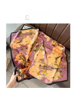 Detail of a large silk-feel scarf with purple floral print on a brown leather surface