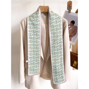 Détail d'un foulard en soie bleu clair à motif mors dorés sur un blazer beige