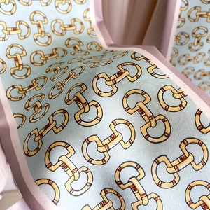 Détail d'un foulard en soie avec imprimé mors doré sur tissu bleu clair et bord rose