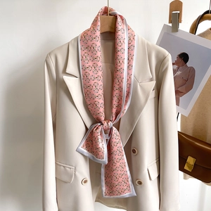 Écharpe fine en soie rose à motif mors de cheval portée sur un blazer blanc cassé élégant