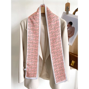 Détail d'un foulard twilly rose à motif mors de cheval sur un blazer beige chic