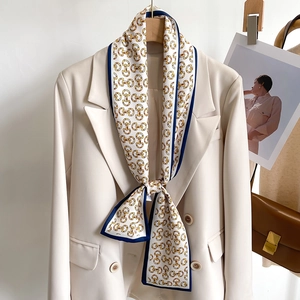 Détail d'un foulard en soie à motif mors doré noué sur le col d'un blazer beige