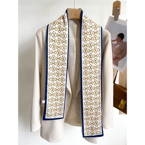 Gros plan d'un foulard en soie long avec imprimé chaîne dorée sur un blazer beige chic