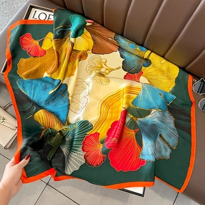 Close-up of silk-like satin square scarf featuring vibrant ginkgo leaf patterns and orange edges
