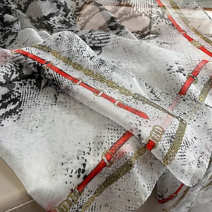 Detail of soft chiffon scarf featuring grey snakeskin print and golden chain motifs