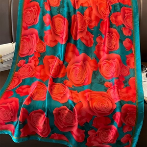 Elegant floral silk scarf with red roses and green border draped on leather surface