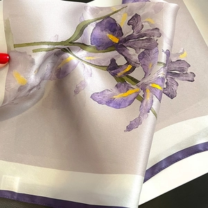 Close-up of a lilac silk scarf with elegant purple iris floral patterns and rolled edges