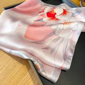 Détail macro d'un foulard en soie rose à motif floral sur un plateau de présentation