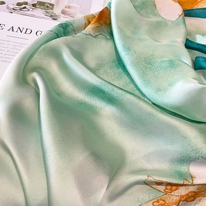 Close-up of mint green silk-like scarf with orange floral pattern and satin texture