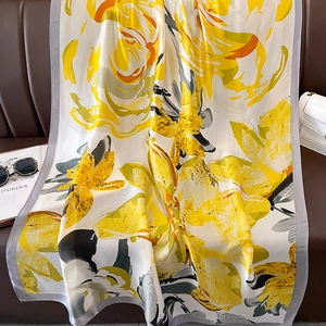 Floral print silk scarf in beige and yellow draped on a leather sofa with lifestyle accessories