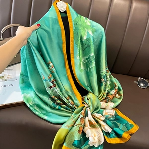 Elegant mint green silk scarf with floral print and yellow borders on a leather sofa
