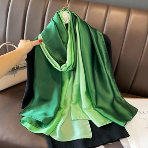 Detail view of smooth green gradient satin silk scarf on a premium leather texture