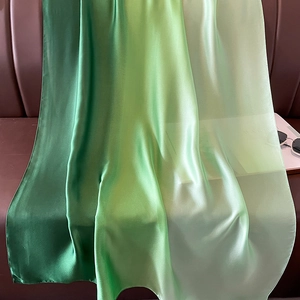 Detail of gradient green satin scarf draped over a brown leather sofa with sunglasses