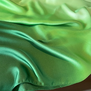 Detailed close-up of smooth satin fabric with elegant ombre green gradient transition