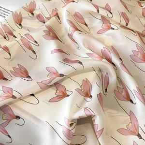 Close-up of lightweight silk scarf featuring elegant pink floral patterns on cream fabric