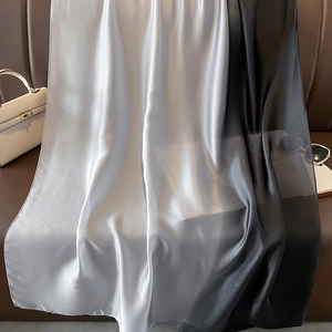Detail of gradient satin silk scarf draped elegantly on a brown leather sofa background