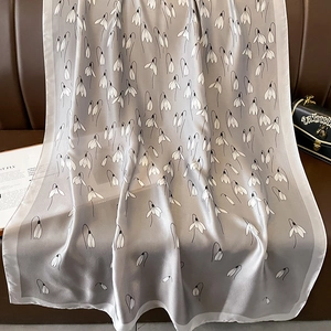 Detail of grey silk scarf with lily of the valley floral print on a leather surface
