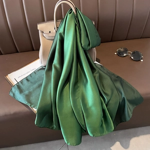 Deep green satin silk scarf draped elegantly over a handbag on a leather sofa