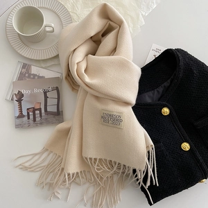 Detail of cream cashmere scarf with brand label, tassels, and premium knit texture