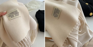 Detailed macro view of cream cashmere-like scarf showing soft fringe and brand label