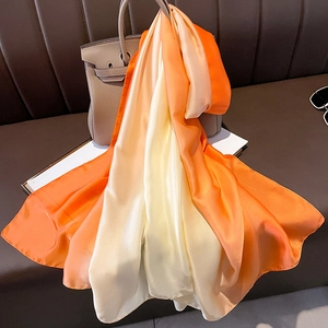 Detail view of smooth gradient silk scarf draped over a luxury handbag in warm lighting