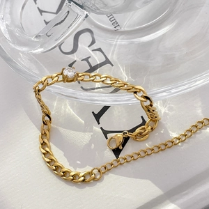Close-up of a gold-plated Cuban chain bracelet with a sparkling round zircon in sunlight