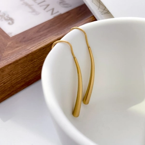 Detail of 18K gold-plated teardrop hook earrings hanging on a white ceramic cup