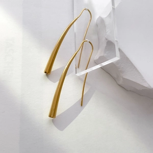 Polished 18K gold-plated long curved hook earrings on a minimalist display